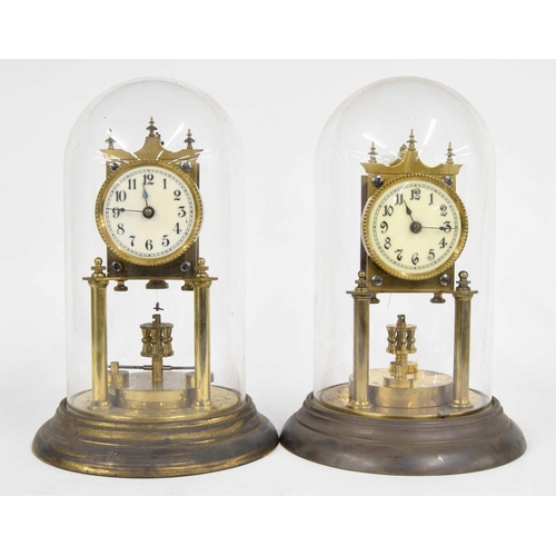 2303 - Two similar brass torsion timepieces with disc pendulums, under glass domes and upon circular steppe... 