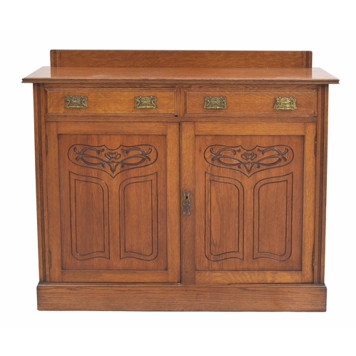 965 - Art Nouveau oak cupboard, the raised back over two drawers with stylised brass handles, over panelle... 