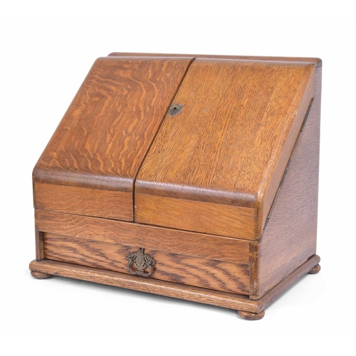 1129 - Early 20th century golden oak slope front stationery box, the double hinged doors enclosing a fitted... 