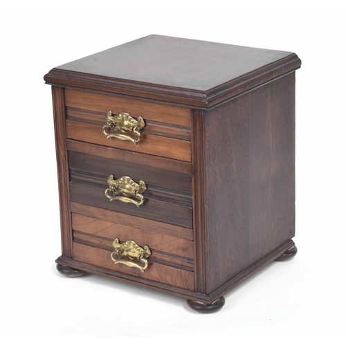 1112 - Edwardian walnut table-top three drawer miniature chest of drawers, with repousse brass handles upon... 