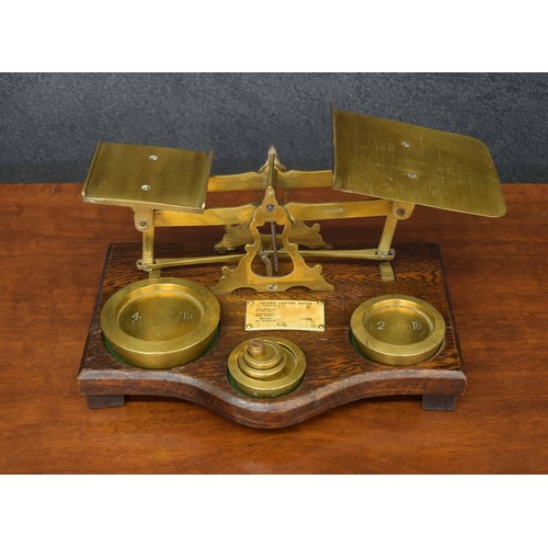 1131 - Set of early 20th century brass postal scales with a serpentine oak base and six weights, applied wi... 