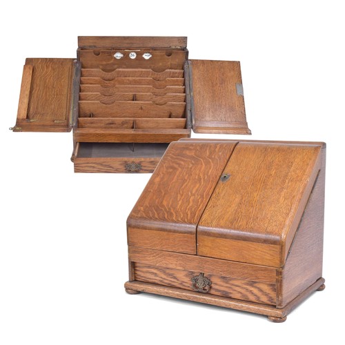 1129 - Early 20th century golden oak slope front stationery box, the double hinged doors enclosing a fitted... 