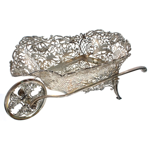 Impressive novelty large silver and plated sweetmeat wheelbarrow dish, the pierced foliate basket cast with birds and floral garlands, on a rotating wheel and two scroll handles / supports, 17" wide approximately, 7.5" high