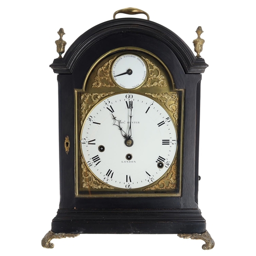 Fine George III ebonised and brass mounted musical triple fusee bracket clock with pull repeat, the 8” arched brass and enamel dial signed Tho’s Hunter, London (Thomas), with a subsidiary tune dial to the arch over the Roman and Arabic numeral dial, with applied cast foliate spandrels, steel hands, the eight day triple chain fusee movement with engraved back plate, later anchor escapement, with musical train and striking on twelve bells, within an ebonised brass mounted arch top case surmounted with a carry-handle over cast metal finials, brass fish grille side panels and brass downswept feet, 19” with the handle raised, 13.5” wide, depth 10” (with pendulum)