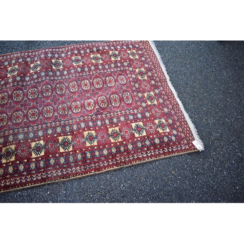 1123 - An Eastern rug, having repeated medallions to central field with geometric borders on a red ground; ... 