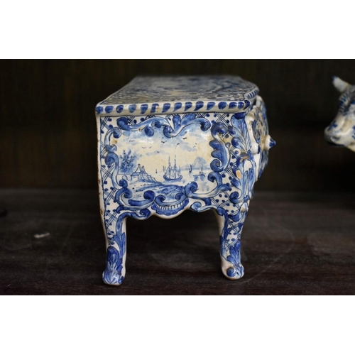 1554 - A Delft miniature commode, 18cm wide; together with another similar cow, 20cm long, (both s.d.).... 