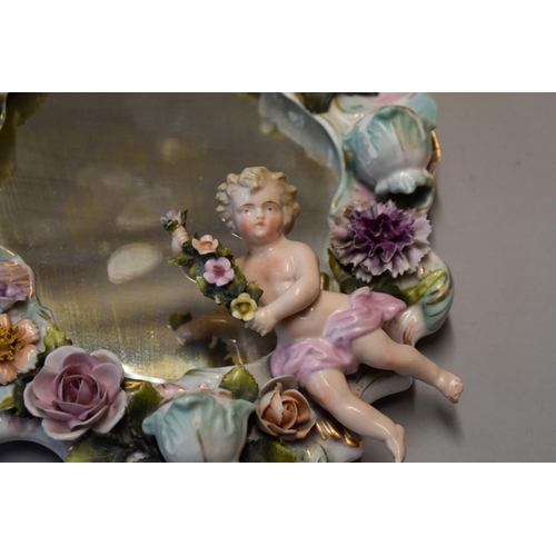 1627 - A Continental porcelain wall mirror, decorated cherub and encrusted flowers, 31cm; together with ano... 