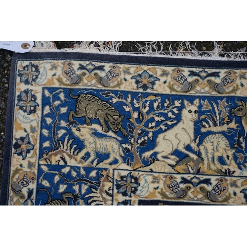 1093a - A Qum silk rug, having central field decorated with trees and animals on a blue ground, with animals... 