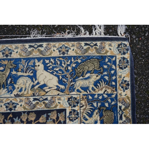 1093a - A Qum silk rug, having central field decorated with trees and animals on a blue ground, with animals... 