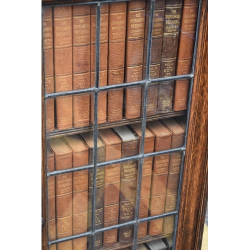 1077 - A 1930s oak slim bookcase, containing a quantity of 1911 Encyclopaedia Britannica books, 36.5cm wide... 