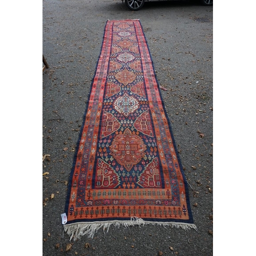 1100 - A long Tribal runner, having seven central medallions, with floral borders on a red and blue ground,... 
