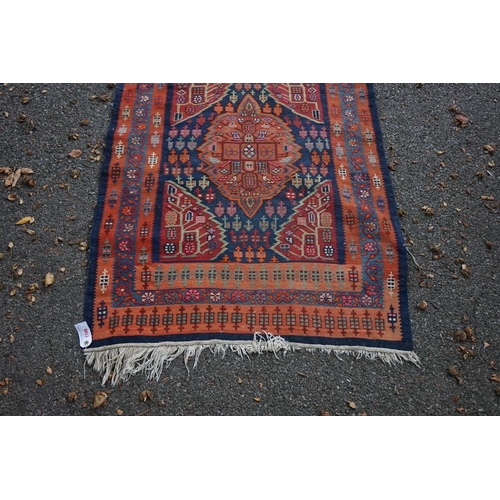 1100 - A long Tribal runner, having seven central medallions, with floral borders on a red and blue ground,... 