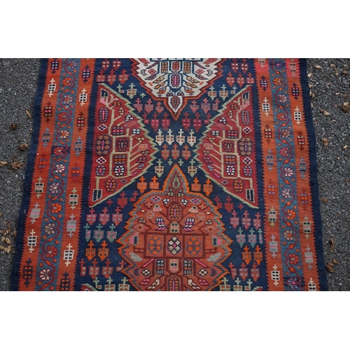 1100 - A long Tribal runner, having seven central medallions, with floral borders on a red and blue ground,... 