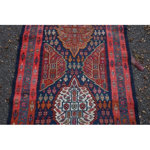 1100 - A long Tribal runner, having seven central medallions, with floral borders on a red and blue ground,... 