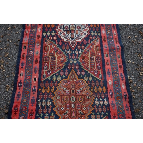 1100 - A long Tribal runner, having seven central medallions, with floral borders on a red and blue ground,... 