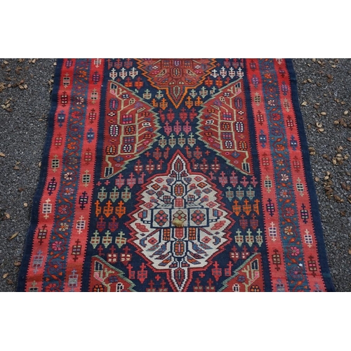 1100 - A long Tribal runner, having seven central medallions, with floral borders on a red and blue ground,... 
