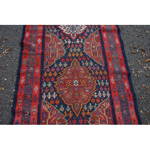 1100 - A long Tribal runner, having seven central medallions, with floral borders on a red and blue ground,... 