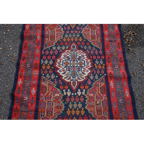 1100 - A long Tribal runner, having seven central medallions, with floral borders on a red and blue ground,... 