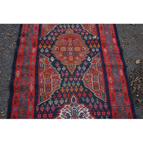 1100 - A long Tribal runner, having seven central medallions, with floral borders on a red and blue ground,... 