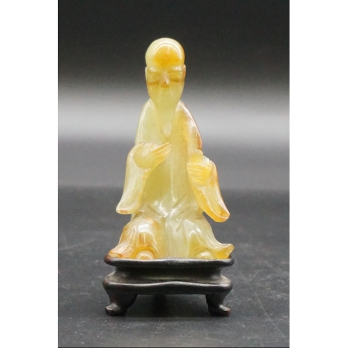 1311 - A Chinese carved mottled green jade seated figure, 8.7cm high, on fitted hardwood stand.... 