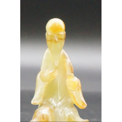 1311 - A Chinese carved mottled green jade seated figure, 8.7cm high, on fitted hardwood stand.... 