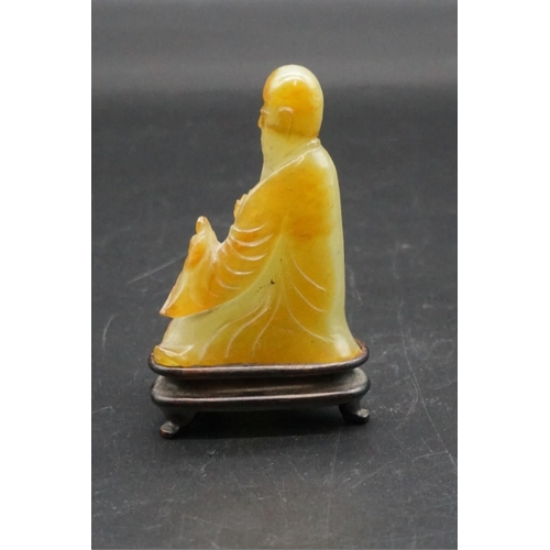 1311 - A Chinese carved mottled green jade seated figure, 8.7cm high, on fitted hardwood stand.... 