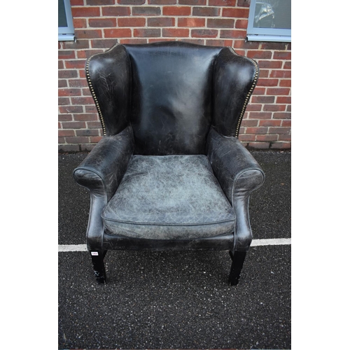 1455 - An 18th century style studded black leather wing armchair, on ebonized legs. 