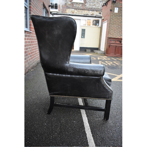 1455 - An 18th century style studded black leather wing armchair, on ebonized legs. 