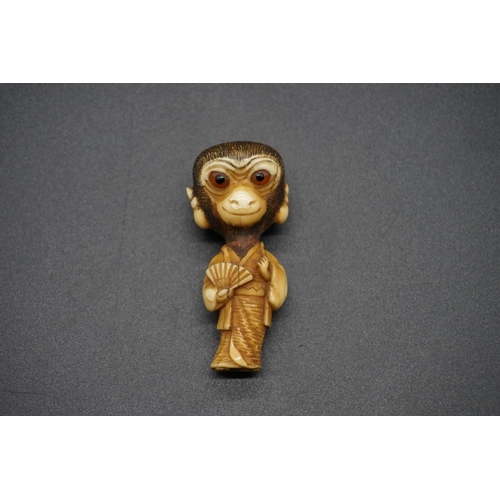 1250 - An unusual Japanese carved ivory netsuke, Meiji, depicting a standing monkey in robes, with inset ey... 