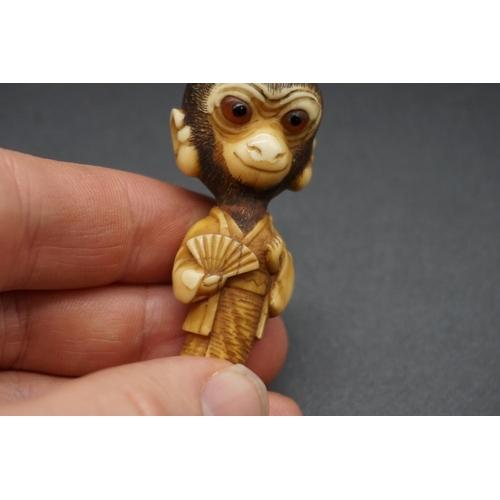 1250 - An unusual Japanese carved ivory netsuke, Meiji, depicting a standing monkey in robes, with inset ey... 