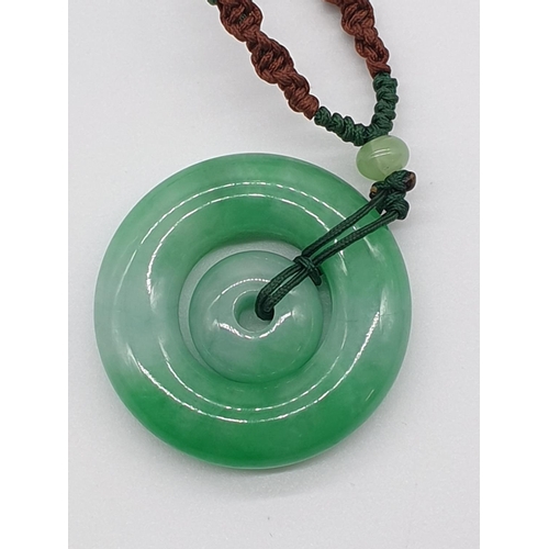 53 - (NB) A jadeite double disk pendant, 45mm diameter, on original silk cord.