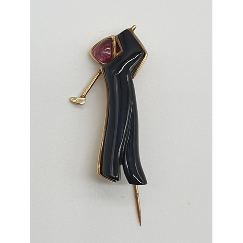 65 - (NB) A yellow metal golfer lapel pin, stamped 585, with carved onyx body and cabochon ruby head, 45m... 