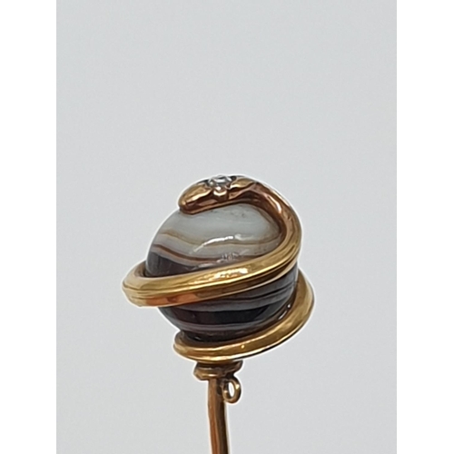 74 - (NB) A 19th century French yellow metal stick pin, terminating in an agate ball decorated coiled sna... 