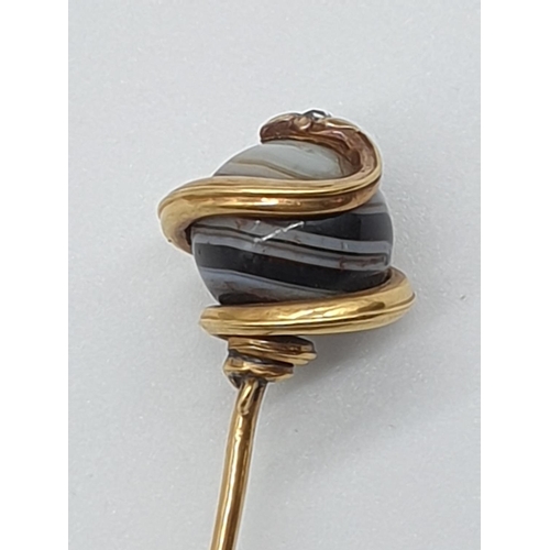 74 - (NB) A 19th century French yellow metal stick pin, terminating in an agate ball decorated coiled sna... 