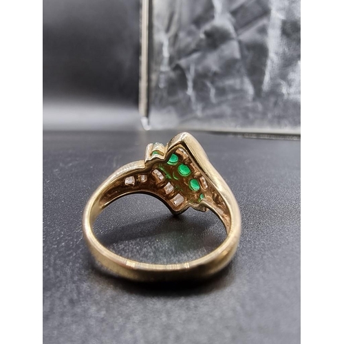 699 - An emerald and diamond crossover ring, set five graduated emeralds, stamped '14Kt', size P.... 