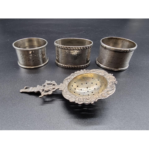 630 - Three various silver napkin rings, 82g; together with a tea strainer, stamped 800.