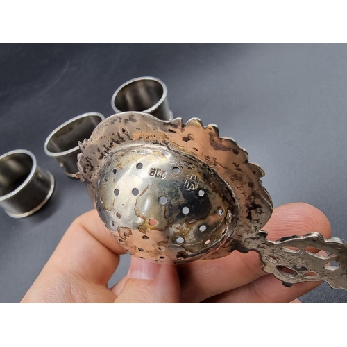 630 - Three various silver napkin rings, 82g; together with a tea strainer, stamped 800.