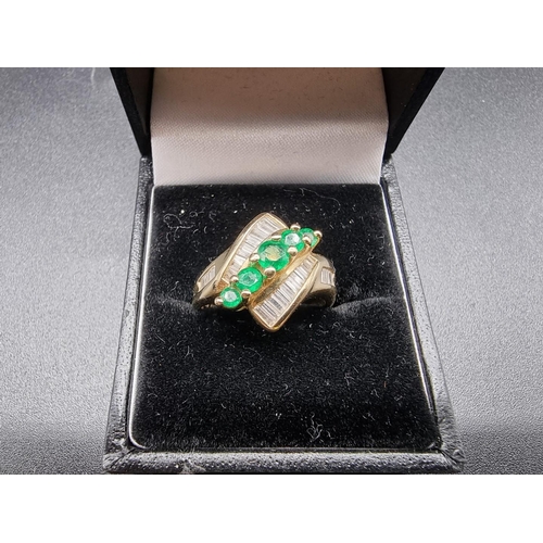 699 - An emerald and diamond crossover ring, set five graduated emeralds, stamped '14Kt', size P.... 