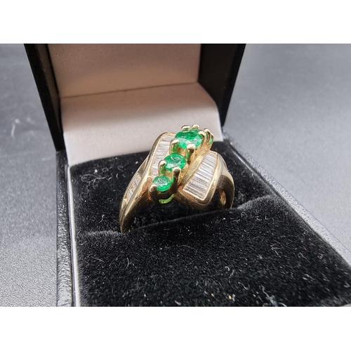 699 - An emerald and diamond crossover ring, set five graduated emeralds, stamped '14Kt', size P.... 