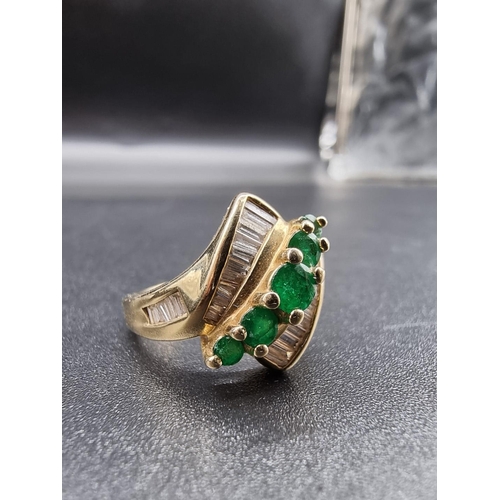 699 - An emerald and diamond crossover ring, set five graduated emeralds, stamped '14Kt', size P.... 