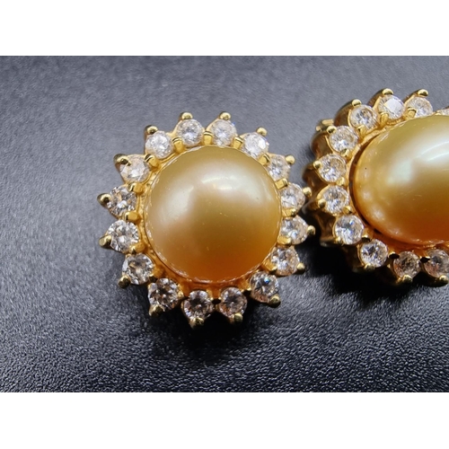 720 - A pair of yellow metal ear clips, set central South Sea golden pearl surrounded by a border of eight... 