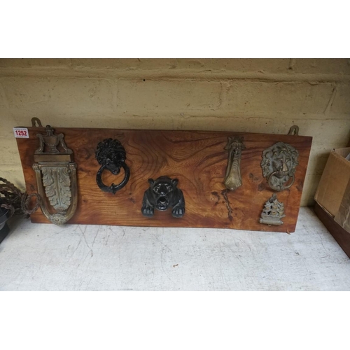 1252 - A collection of vintage door knockers, mounted on elm plinth, 67cm wide. 