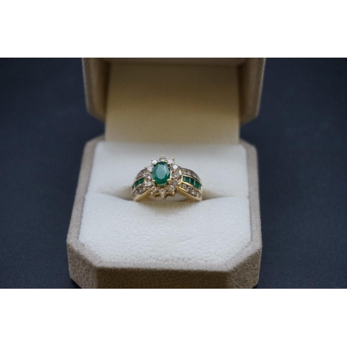 671 - A yellow metal emerald and diamond cluster ring, set central oval emerald surrounded by twelve brill... 