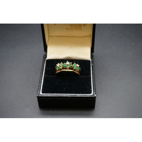 700 - An emerald and diamond ring, stamped 18, set three emerald and diamond floral clusters, size O1/2.... 