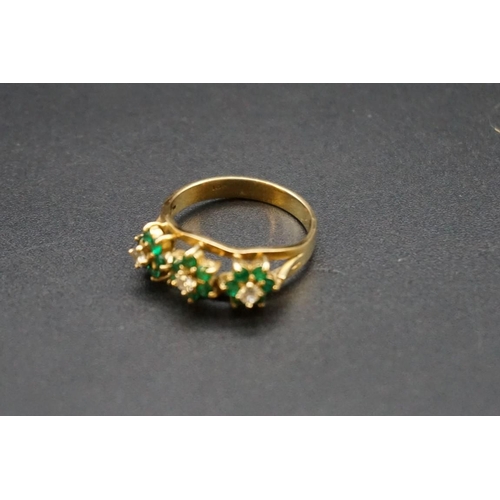 700 - An emerald and diamond ring, stamped 18, set three emerald and diamond floral clusters, size O1/2.... 