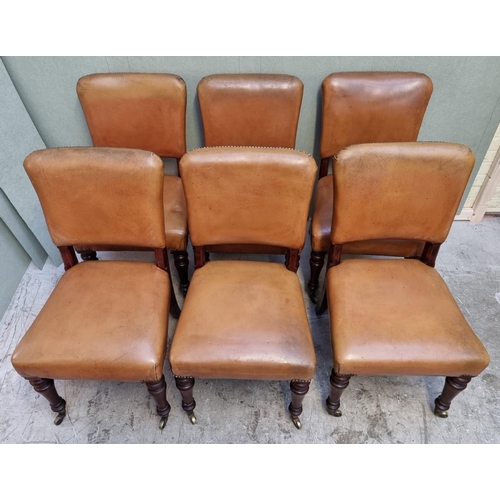 1086 - A set of six mahogany and studded tan leather side chairs, with brass caps and casters to the f... 