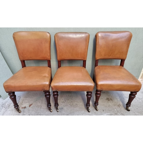 1086 - A set of six mahogany and studded tan leather side chairs, with brass caps and casters to the f... 