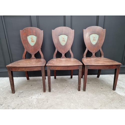 1075 - An interesting set of three George III shield back hall chairs, each with painted lion crest to back... 