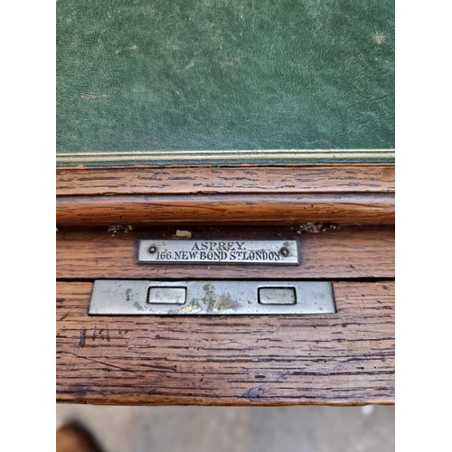 1064 - An unusual early 20th century oak writing table, by Asprey, the hinged top revealing a rising leathe... 