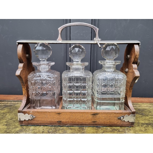 1185 - An oak and silver plate three bottle tantalus, 31.5cm wide, (bottles mismatched). ... 